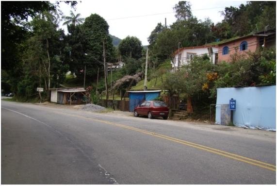 Fotografia 90: Moradias ao longo da Estrada-Parque, na encosta de morro, na Serra do Guararu, e materiais de construção ao lado do acostamento, indicando reforma ou possibilidade de nova edificação em área tombada.