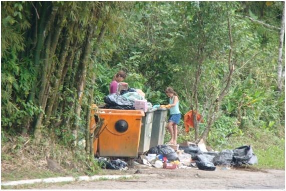 Fotografia 82: Essa foto foi tirada de longa distância, para não constranger. Retrata caçambas de lixo ao longo da Estrada-Parque da Serra do Guararu, com crianças manuseando diretamente o lixo em busca de objetos com algum tipo de interesse.
