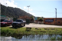 Fotografia 10: Valeta de drenagem com água poluída, loja de material de construção e maciço da Serra do Guararu ao fundo.